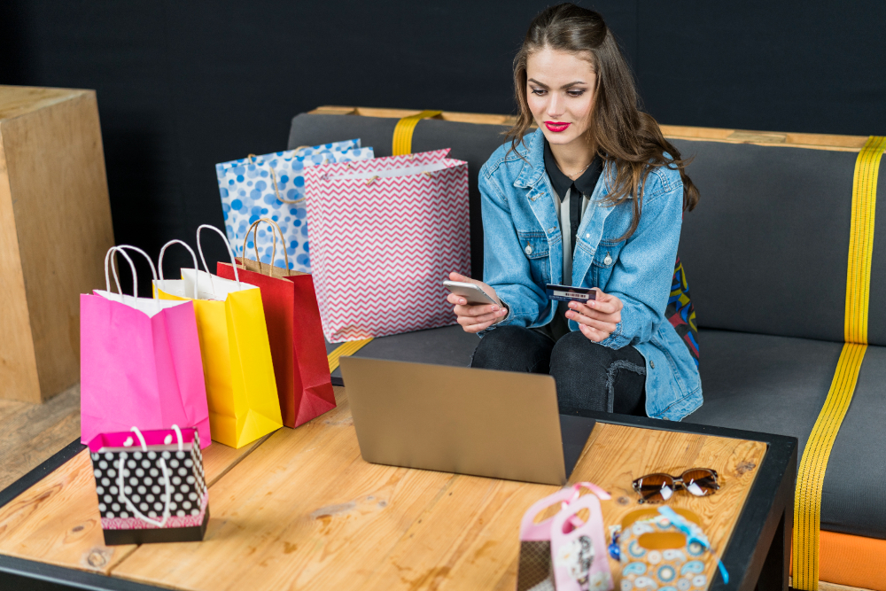 Beautiful woman sitting at home with electronic devices; marketing bags and credit card in hand