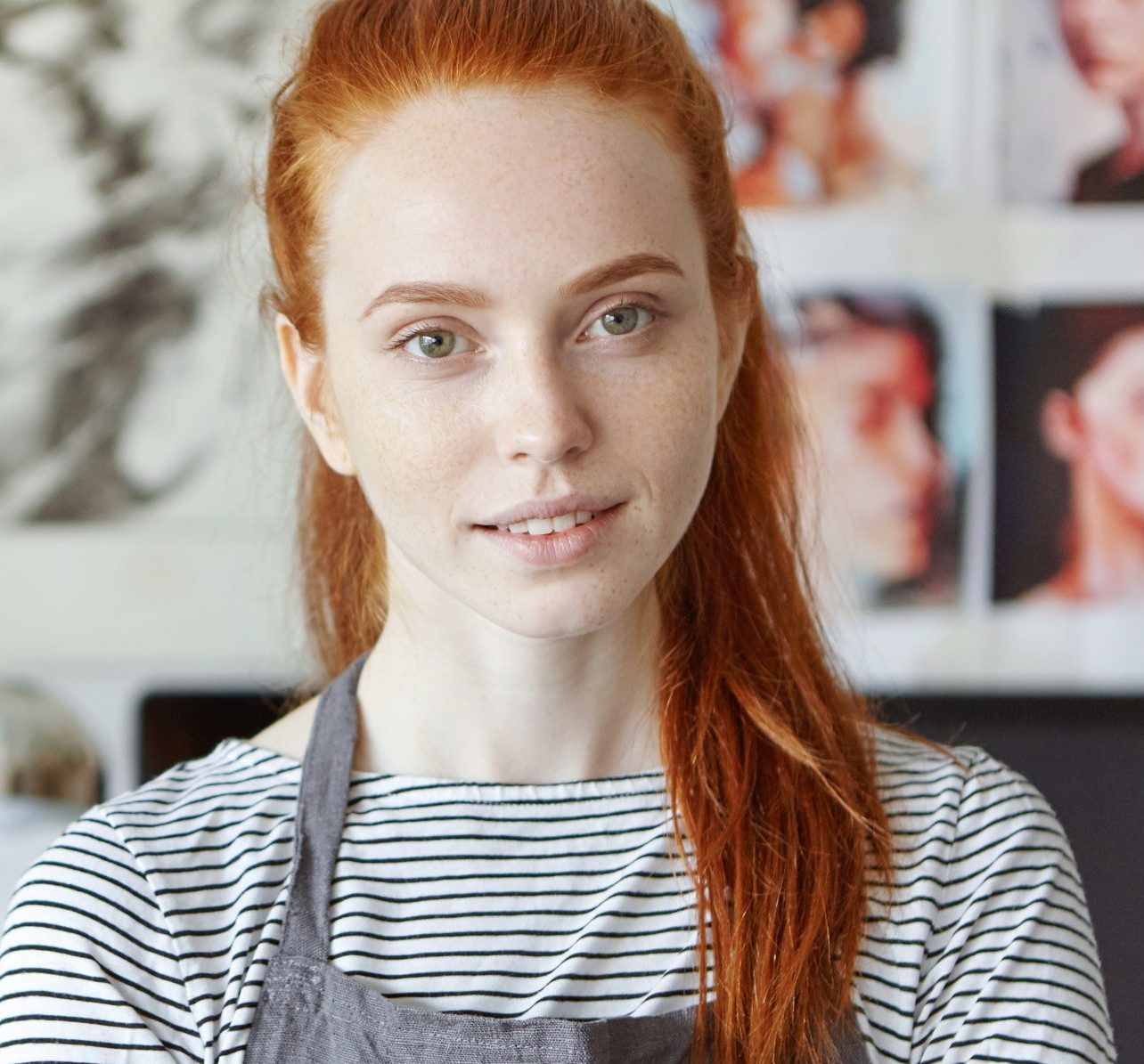 confident-charming-young-female-digital marketer wearing striped top grey-apron posing her studio for profile picture