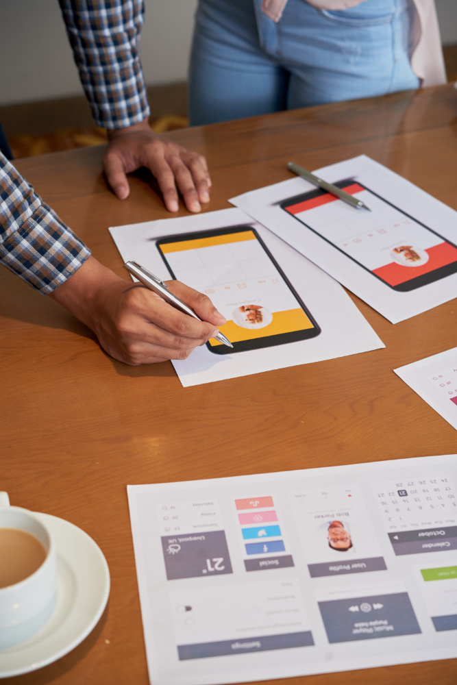 Unrecognizable colleagues standing at table and looking at mobile website development projects