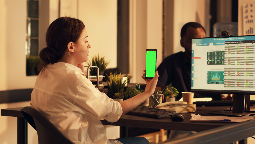 Office worker looking at applocation development template on mobile phone, using isolated mockup background and stock market trade statistics. Working with blank copyspace on smartphone with react native application. Tripod shot.