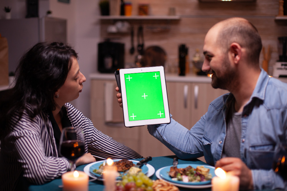 Couple using tablet pc with chroma key and enjoying their time together during romantic dinner. Husband and wife looking at green screen template chroma key display web design sitting at the table in Resturant